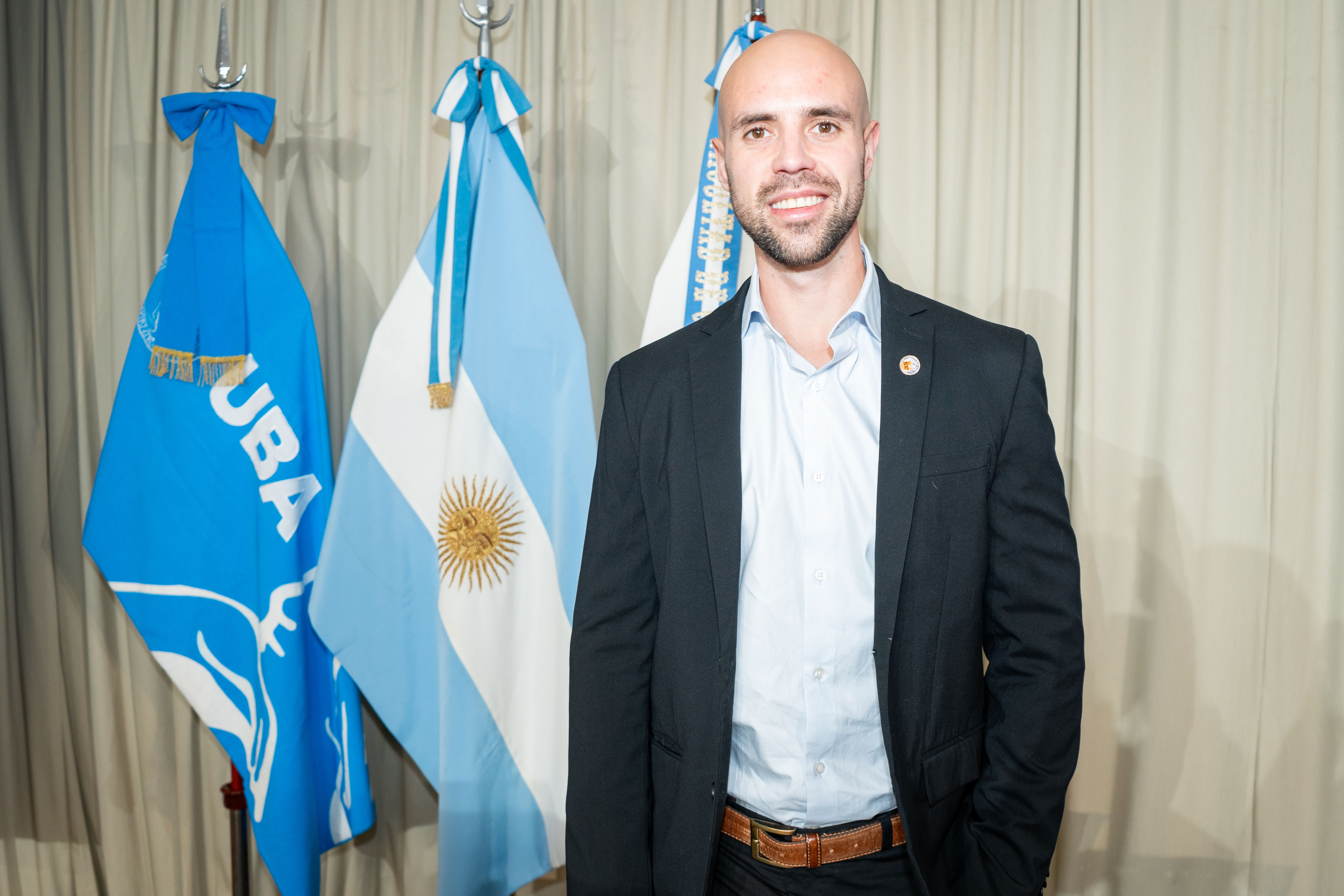 Juan Aranovich standing in a suit in front of Argentine flags